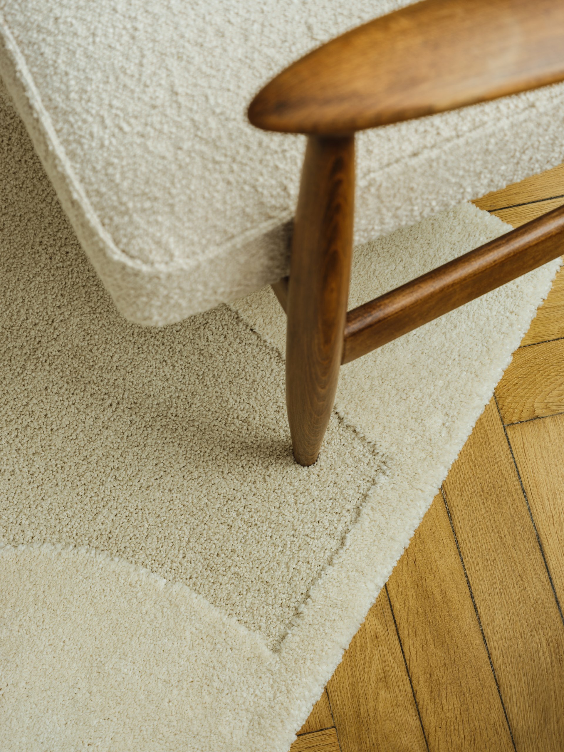 Close-up of a wooden armchair with soft boucle fabric and a textured rug